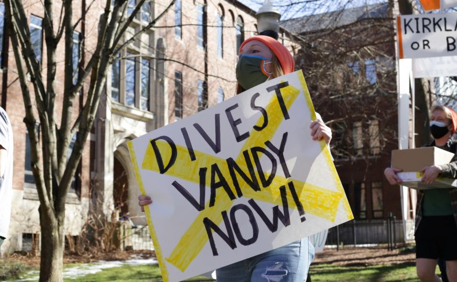 woman holding white sign that reads "divest vandy now" with a yellow X over the front